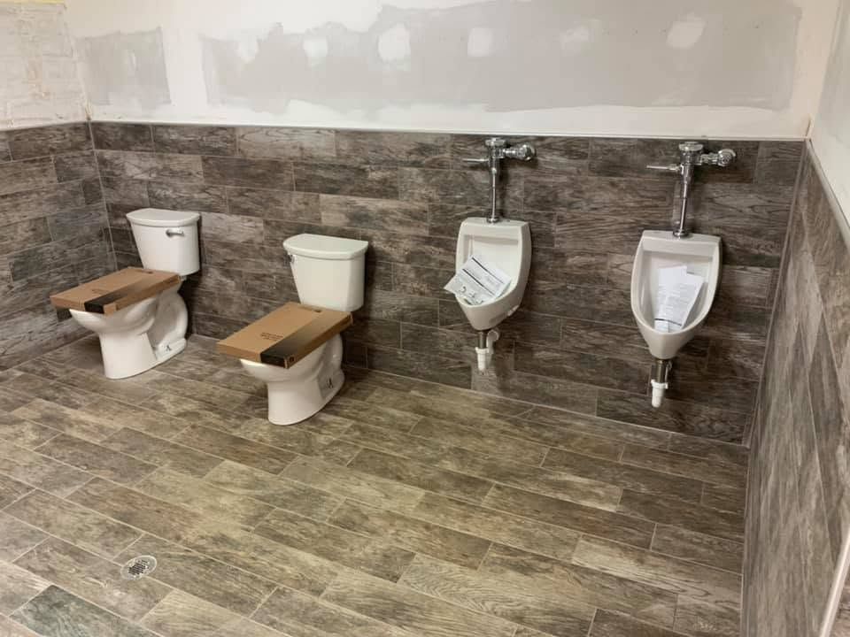 Two newly set toilets and two urinals with flush valves on a tiled restroom wall